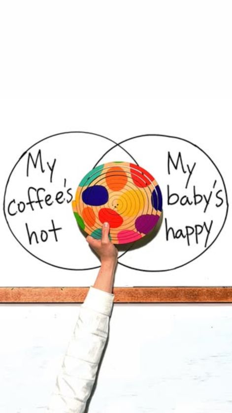 Hand-drawn Venn diagram on a whiteboard, “My coffee's hot” and “My baby's happy”, with an arm holding a colourful Lovevery wooden toy over the overlap