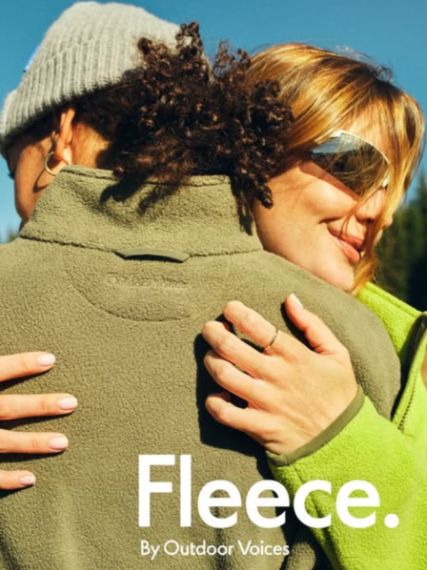 Two people hugging outdoors, one in a sage Outdoor Voices fleece, with large white text “Fleece. By Outdoor Voices”