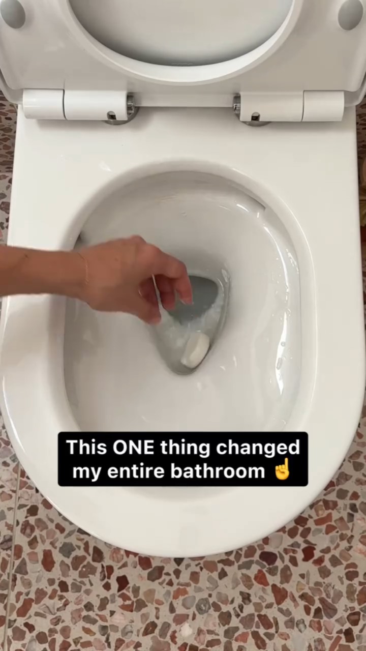 Top-down view of a white toilet bowl as a hand drops in a cleaning tablet, captioned “This ONE thing changed my entire bathroom ☝️”