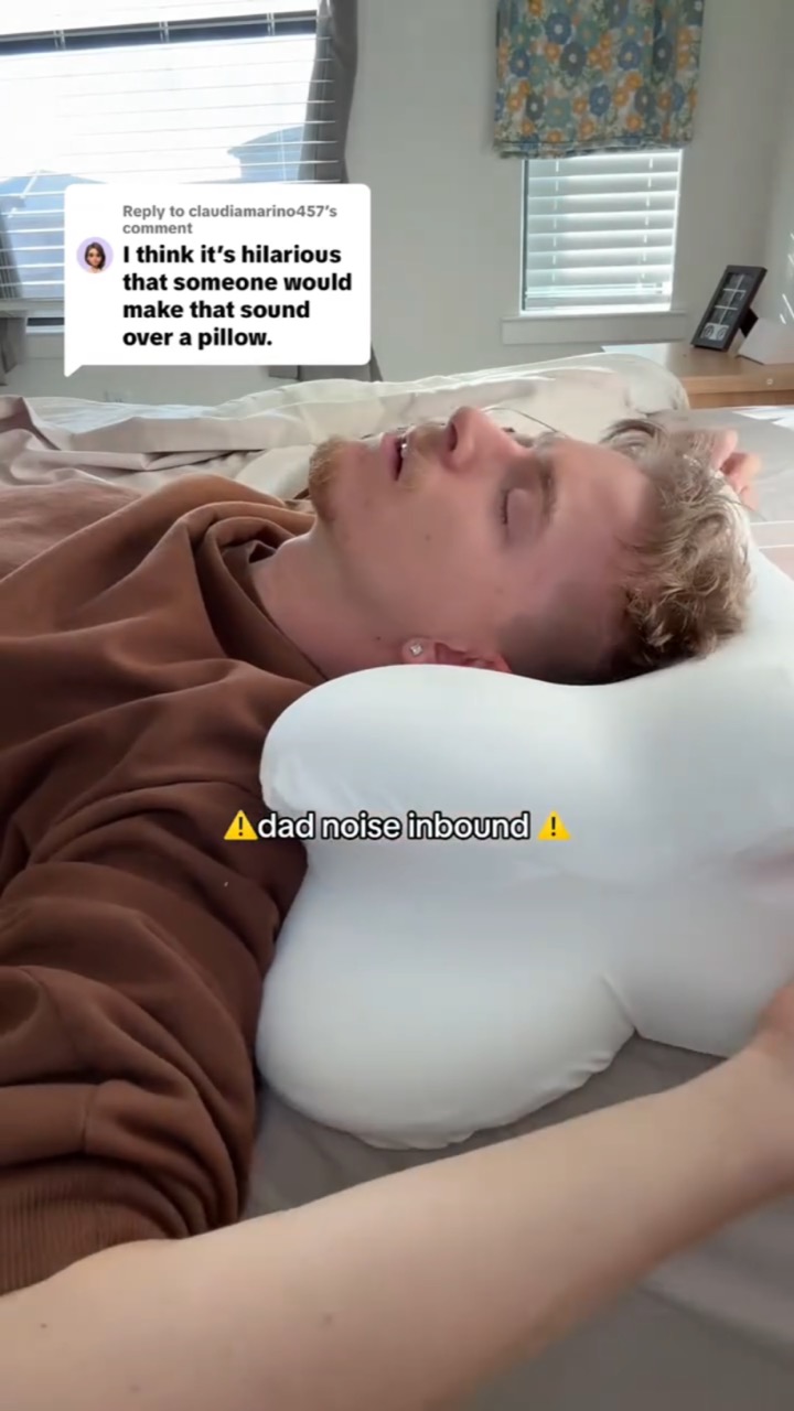 A man lies back on a white contoured cloud pillow under a comment sticker “I think it’s hilarious that someone would make that sound over a pillow.”, captioned “⚠️dad noise inbound ⚠️”