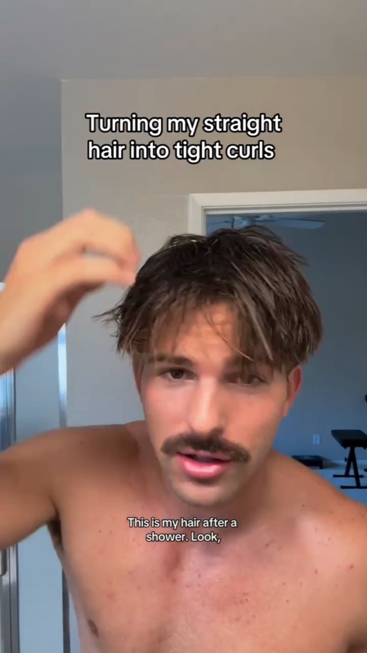 A shirtless man with a mustache runs a hand through damp straight hair under the caption “Turning my straight hair into tight curls”, subtitled “This is my hair after a shower. Look,”