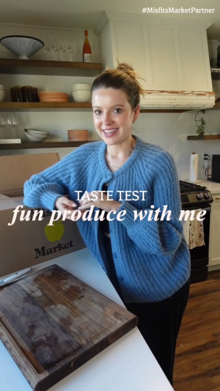 A smiling creator in a blue cardigan leans on her kitchen counter beside a Misfits Market box and cutting board, captioned “TASTE TEST fun produce with me” with a #MisfitsMarketPartner tag
