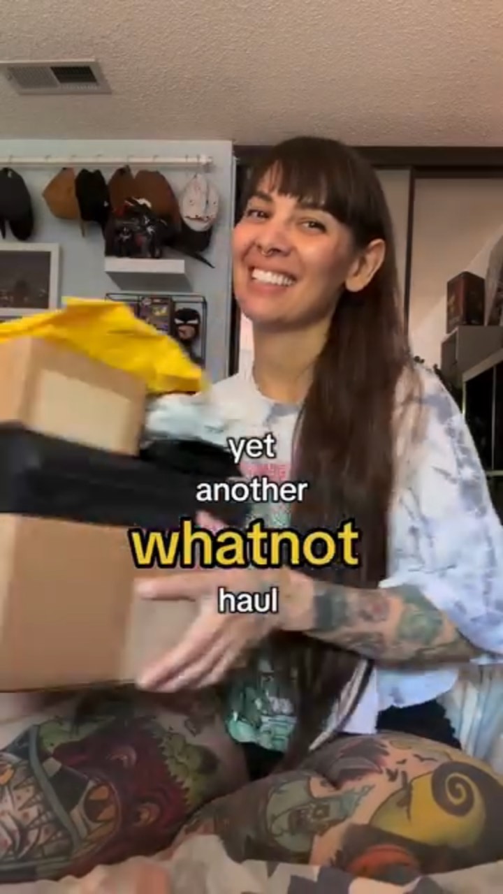 A smiling tattooed creator on her couch lifts a stack of Whatnot mailer boxes, captioned “yet another whatnot haul”
